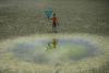 Image of a boy looking at a pool in a dried-up reservoir in Bangladesh   